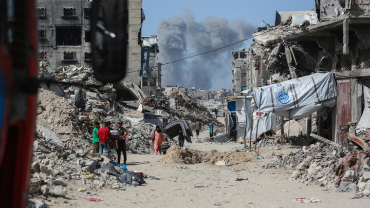 Smoke billows as Palestinians move with their belogings through Jabalia while fleeing the northern Gaza Strip on May 19, 2025.