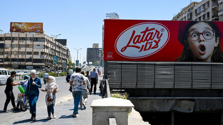 People walk past a chocolate advertisement in the Syrian capital in Damascus on May 20, 2025.