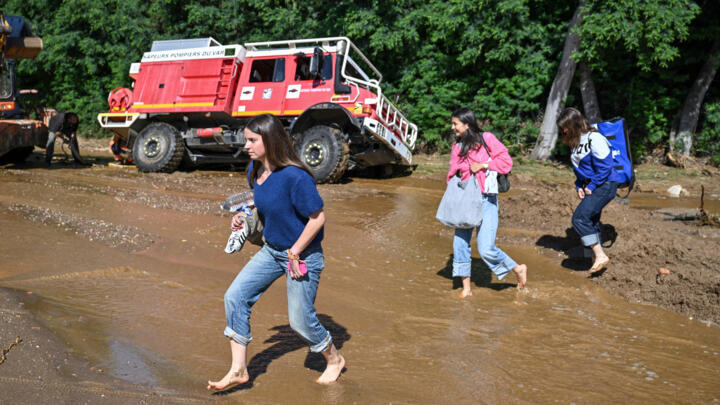 People walk through the water to cross amud-covered road as a firefighting vehicle gets stuck in the mud following a flood caused by heavy rain in Cavaliere village of Le Lavandou commune in the Var d