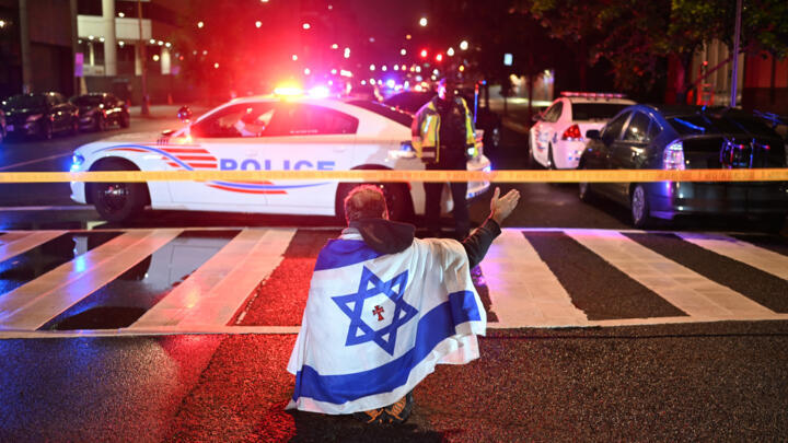 A man draped in the Israeli flag, bearing a cross and the name "Jesus" at its center, at the site of the shooting outside the Capital Jewish Museum on May 22, 2025.