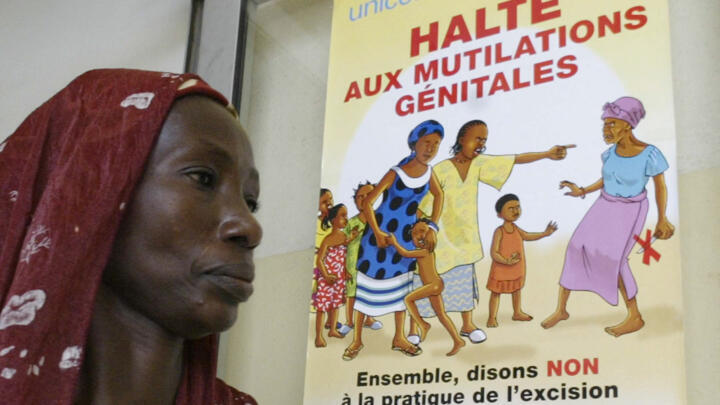 A woman who performs genital cutting passes by a poster supporting the abolition of female genital mutilation during a gathering to denounce excision on November 17, 2005 in Abidjan. 