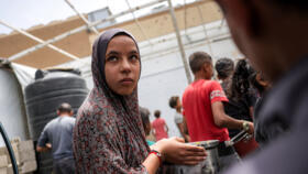 A girl stands with a pot as people queue to receive charity meals from a kitchen in Beit Lahia in the northern Gaza Strip on April 24, 2025. 