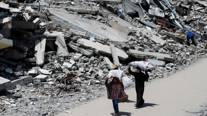A Palestinian woman and a girl carrying bags of firewood walk by the rubble of houses, in Gaza City, May 20, 2025. 